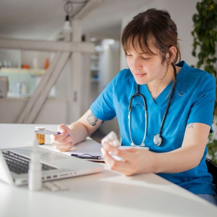 Psychiatric nurse practitioner reviewing medication bottle while working at laptop.